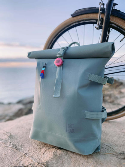 Roam smart finder attached to a stylish grey backpack next to a bike by the beach at sunset.