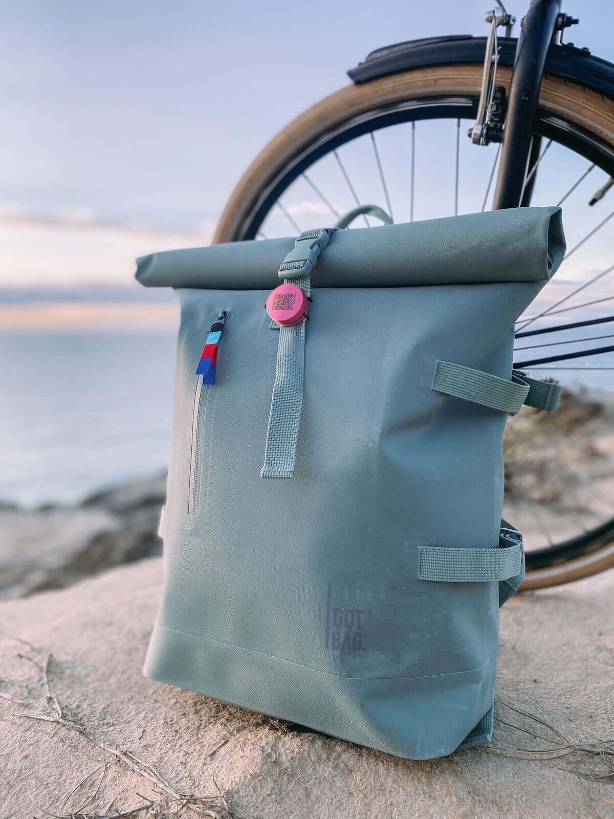 Roam smart finder attached to a stylish grey backpack next to a bike by the beach at sunset.