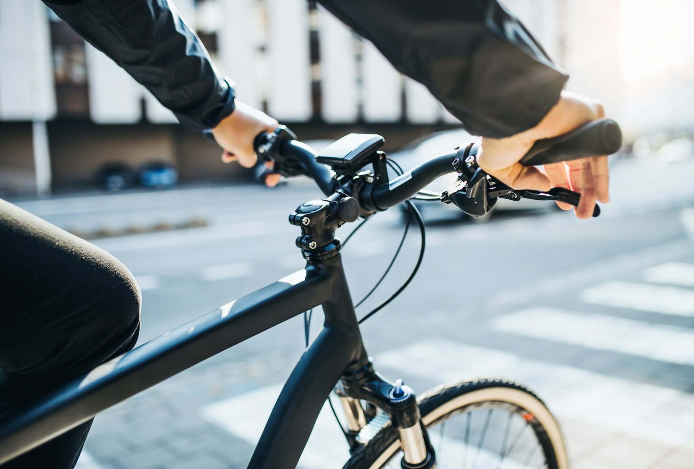 Close-up of a cyclist’s hands gripping the handlebars of a sleek black bicycle, with a Roam Smart Tag attached, ensuring the bike is never lost.